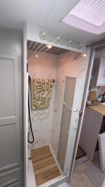 A revamped caravan shower with marble-effect walls, a wooden slatted floor, and a patterned towel hanging.