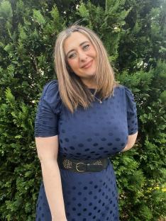 Woman in a navy polka dot dress standing in front of a green bush.