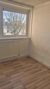 Empty room with wood-look flooring, radiator, and window showing a street scene.