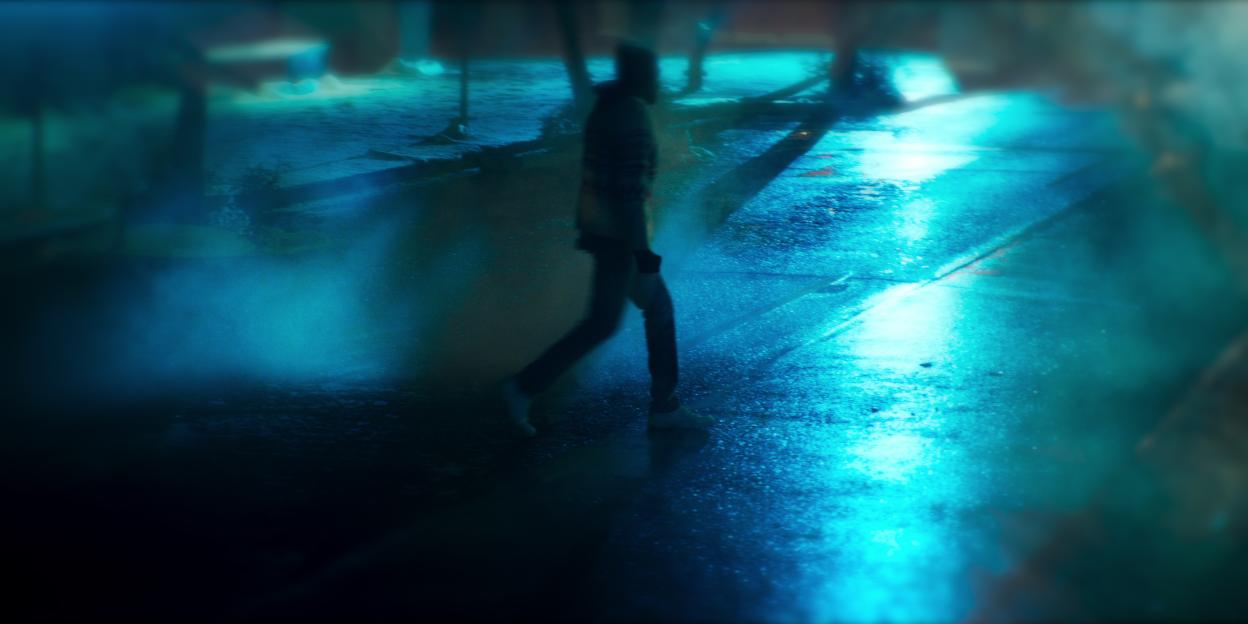 Blurry image of a person walking at night in the rain.