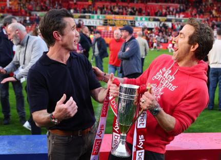 Rob McElhenney and Ryan Reynolds celebrating with a trophy.