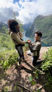 A man proposing to a woman on a mountain overlooking a fjord.