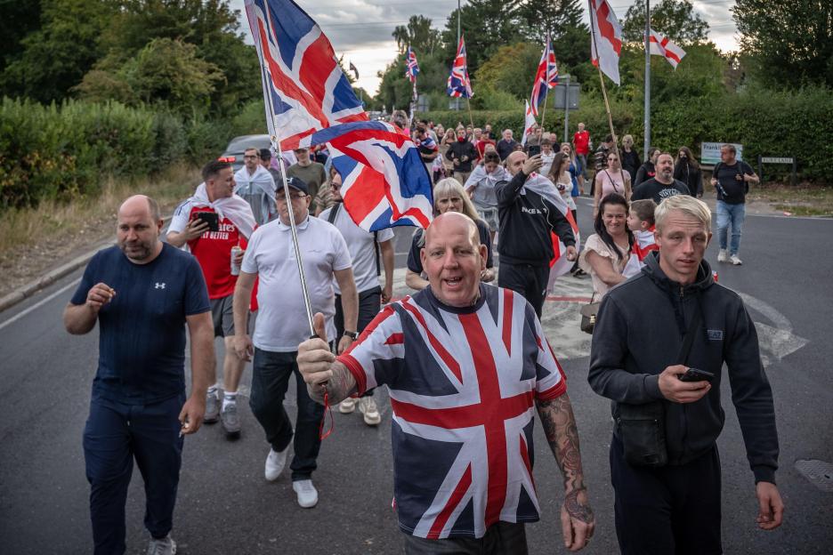 Anti-migrant protesters march through Epping, UK, carrying Union Jack flags.