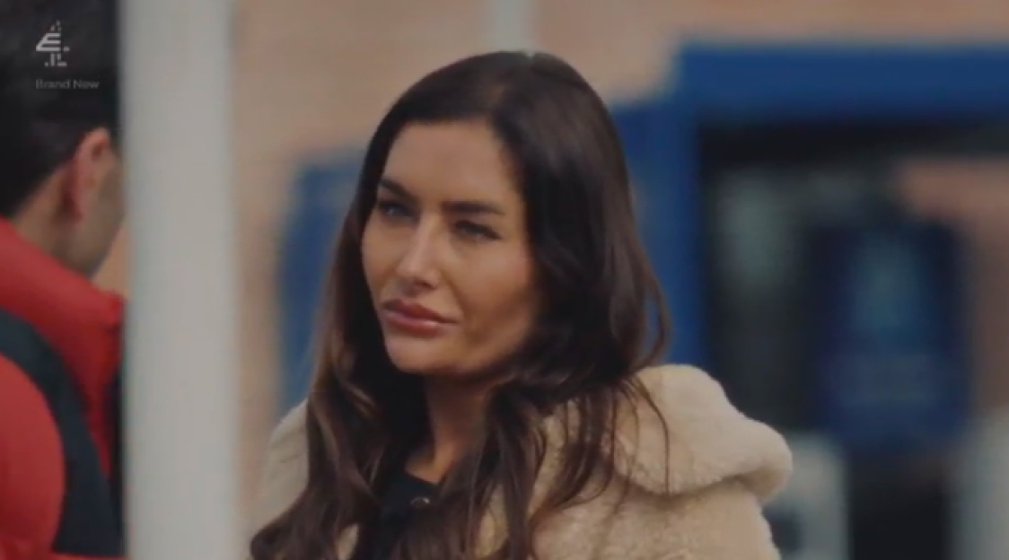 Leisha, wearing a cream coat, tearfully looks towards her groom, Reiss, who is visible from the back.