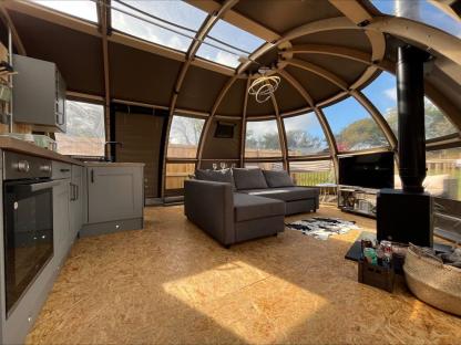 Interior view of a luxury glamping dome tent with kitchen, seating area, and wood-burning stove.