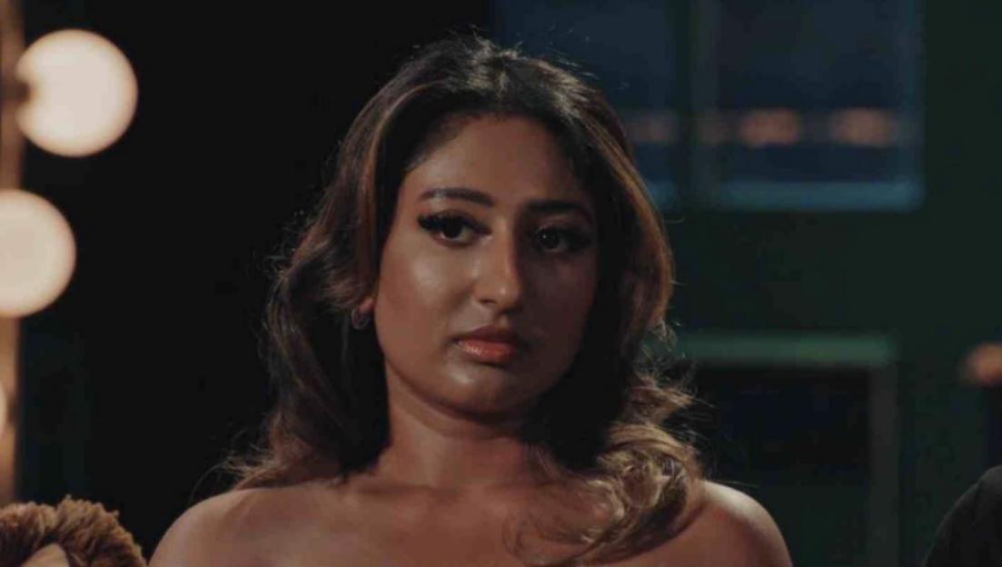 Nelly with long brown hair, wearing an off-the-shoulder top, looking forward.