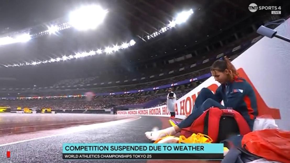 A female athlete sits on a red bag on a track as a broadcast announces the suspension of the World Athletics Championships Tokyo 25 due to weather.