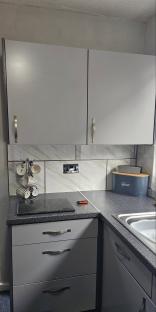 Grey kitchen cabinets and countertops with mugs and a bread bin.