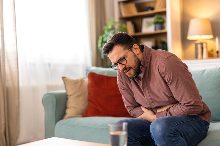 A man sitting on a couch, holding his stomach in pain.