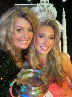 Mother and daughter beauty pageant contestants, one wearing a crown and holding a trophy.