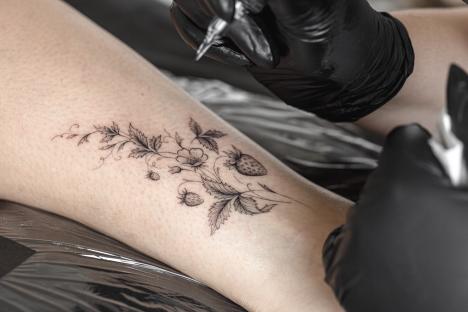 Close-up of a tattoo artist inking a strawberry and flower design on a person's arm.