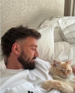 Man with a new hairstyle lying in bed with a cat.
