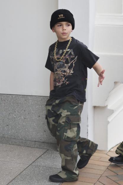 Reign Disick walking in camouflage pants, a black t-shirt, a gold chain, and a black beanie.