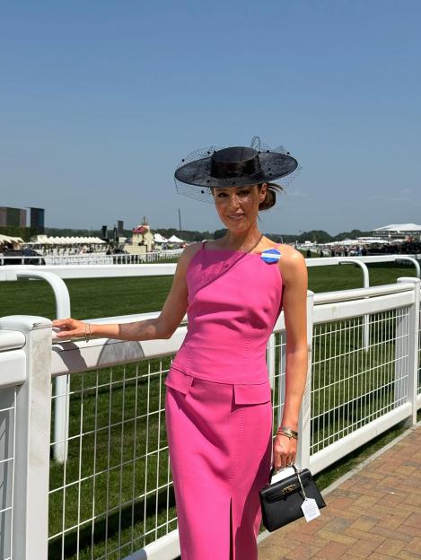 Lorna Luxe wearing a fuchsia dress and a black veiled hat at a racetrack.