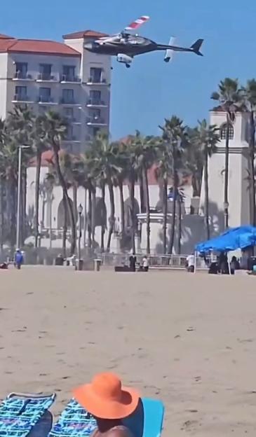 A helicopter flying over a building surrounded by palm trees.