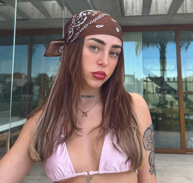 Nicki Nicole wearing a brown bandana, pink bikini top, and a necklace that reads "Bullshit."