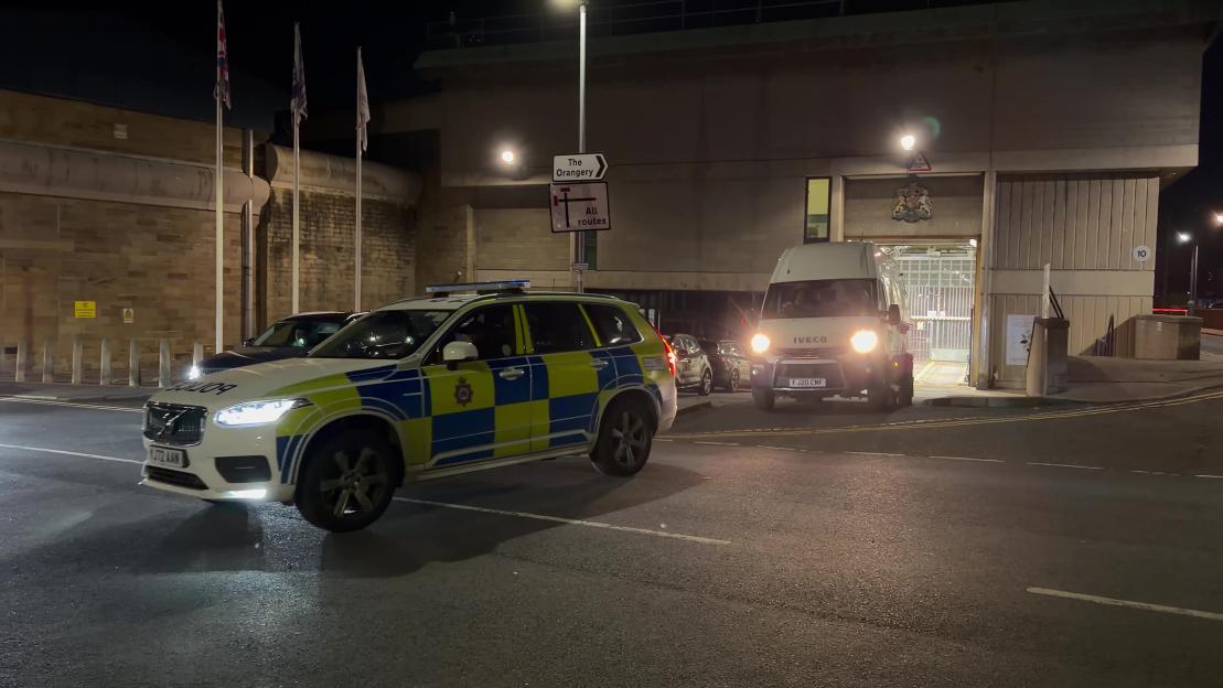Police car and prison van leaving Wakefield prison at night.