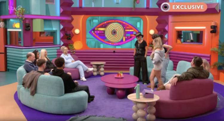 People gathered in a brightly colored room with a large screen displaying the "Big Brother" eye logo.