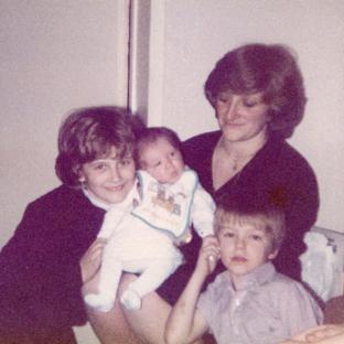 Photo of a woman holding a baby, with two older children beside her.