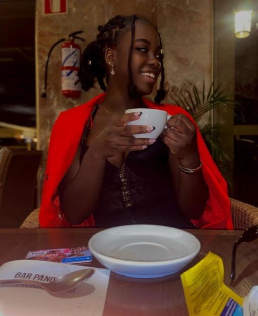 Woman in red jacket sitting at a table, holding a coffee cup.