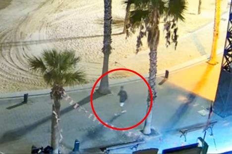 CCTV image of a person walking on a paved area near a beach at night.