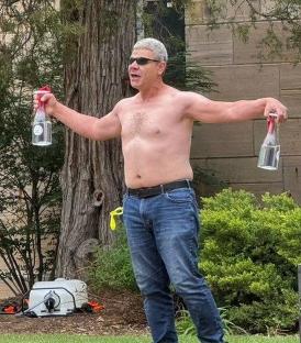 Shirtless man holding two bottles.