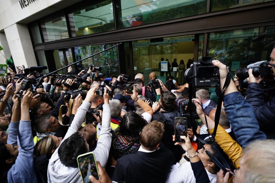 A crowd of photographers and fans surround a person entering a building.