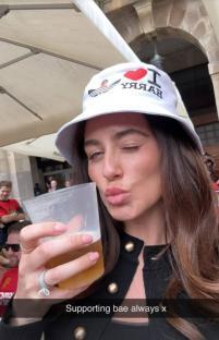 Woman wearing a bucket hat drinking beer and winking.