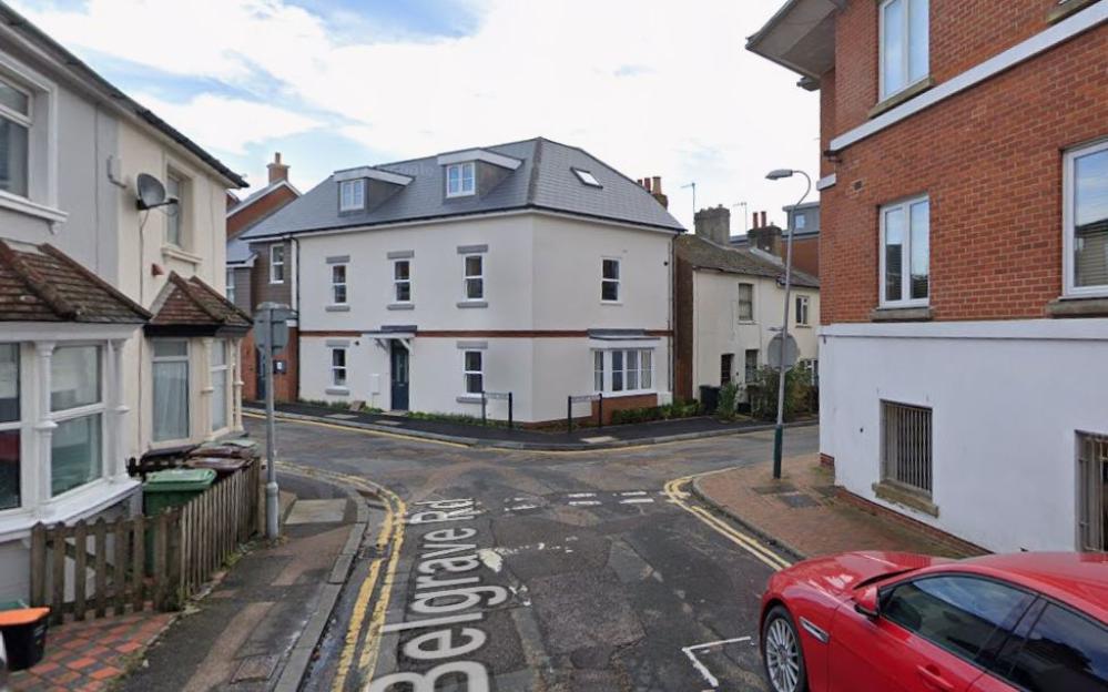 Street view of Belgrave Road featuring a corner building and a red car parked nearby.