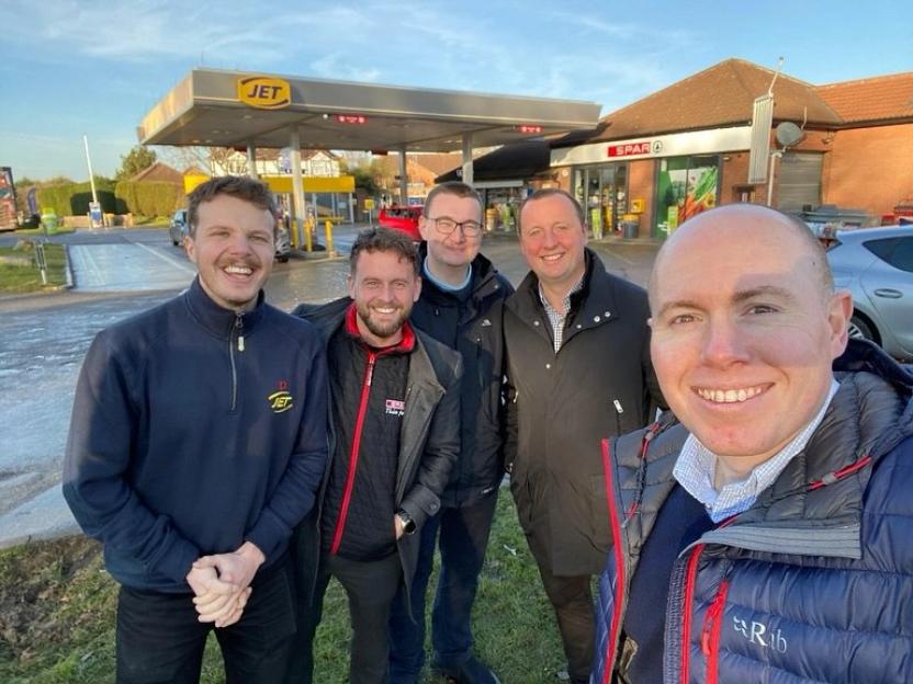 Five men smiling in front of a JET gas station and a SPAR convenience store.
