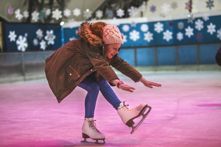 A girl in a winter coat and hat ice skating.