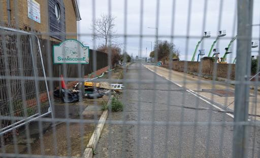 A closed road in Swanscombe, Kent, viewed through a chain-link fence.