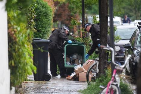 Two police officers searching through a bin and discarded packages on a residential street.