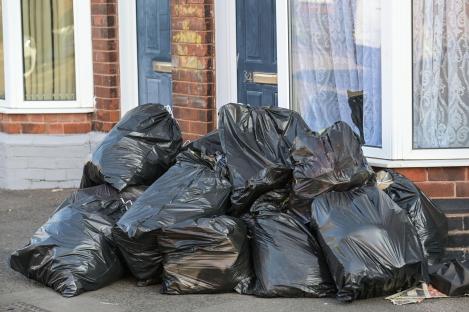 Pile of black garbage bags outside a house.
