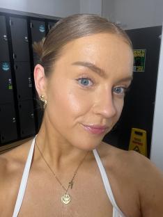 Woman with blonde hair wearing a white top and gold necklace.