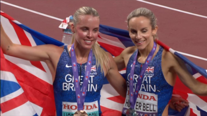 Two Great Britain track athletes holding a British flag and wearing medals.