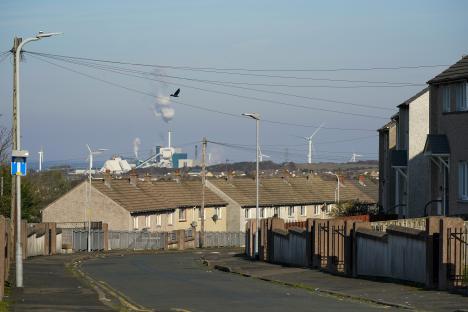 Street scene in Workington, England, showing terraced houses, a factory in the distance, and wind turbines on the horizon.