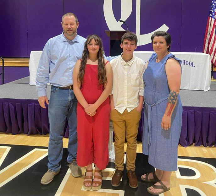 Elijah Heacock and family in front of a purple wall with a large white "C" logo.