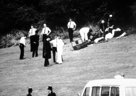 Black and white photo of forensic experts at a crime scene in a wooded area.