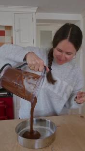Person pouring chocolate cake batter into a cake pan.