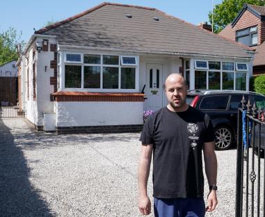 A man stands in front of his house, which is bisected by an HS2 construction site.