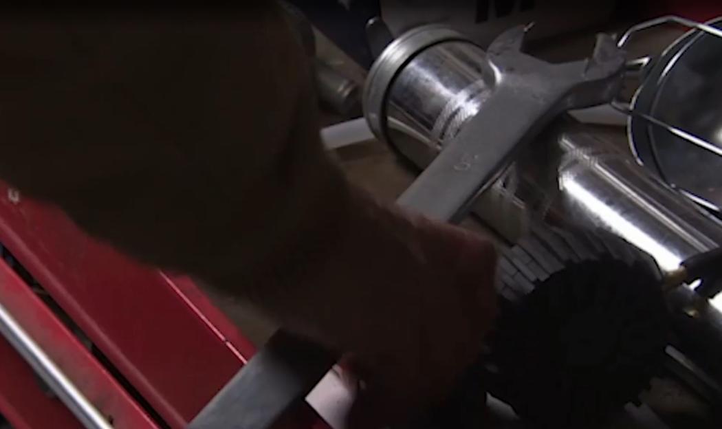 A person's hand using a wrench on a piece of machinery.