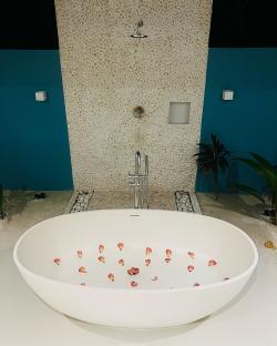 Oval bathtub with flower petals, in a bathroom with pebble tile walls.
