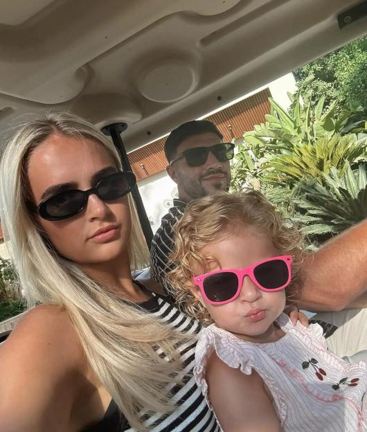 Molly-Mae Hague, a man, and a toddler in sunglasses sitting in a golf cart.