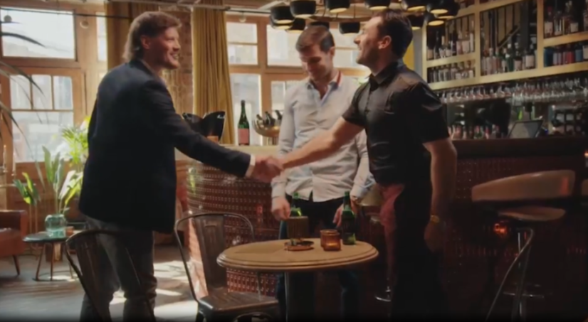 Two men shaking hands in a bar, while another man watches.