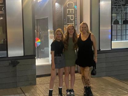 Woman and two girls posing outside a building.