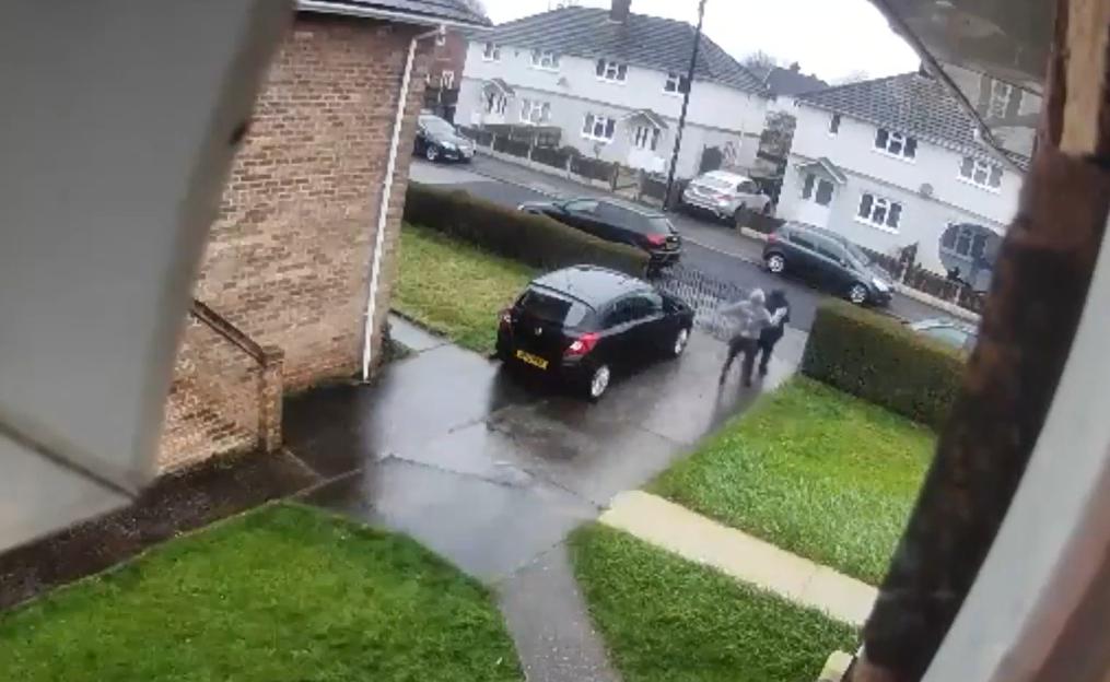 Security camera footage of two people near a car in a driveway.