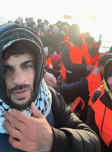 A man in a crowded migrant boat makes a selfie video.