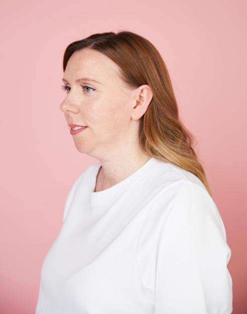 Woman in profile view wearing a white shirt against a pink background.