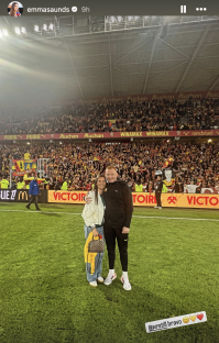 Couple posing on a soccer field in front of a stadium full of spectators.